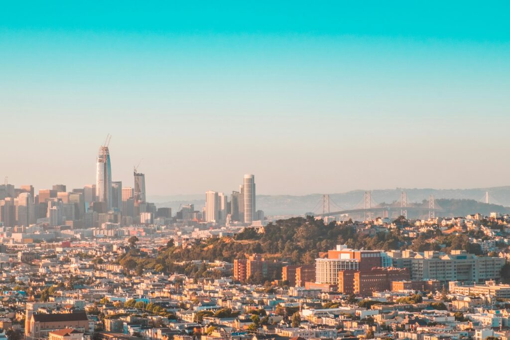 A stunning aerial view of the San Francisco skyline, showcasing modern skyscrapers and the iconic Bay Bridge under a clear daytime sky.